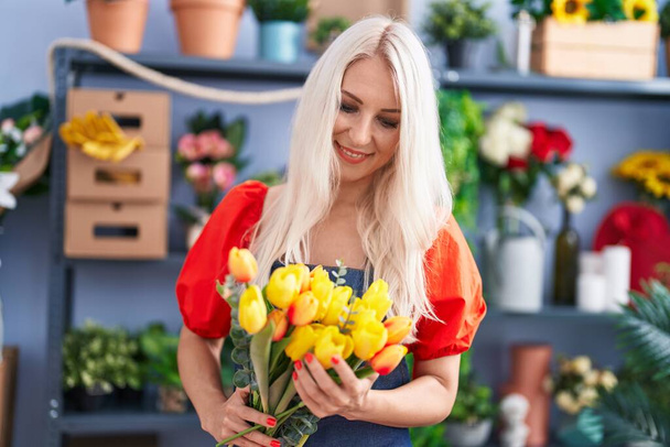 Молодая блондинка-флористка держит букет цветов в цветочном магазине - Фото, изображение