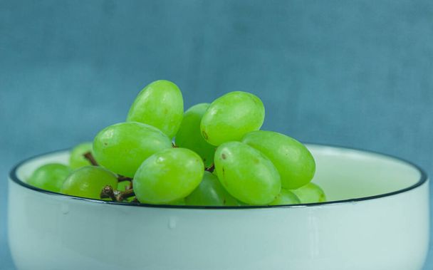 Fresh green grapes in a white porcelain bowl. The image shows a partial close-up of the green grapes. Delicious tasting grapes - Photo, Image