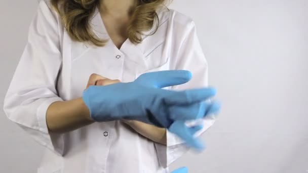 Woman in white robe smock put on blue rubber gloves on her hands - Filmagem, Vídeo