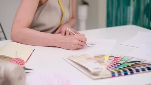 koele vrouw jurk maker met tatoeage tekent kleding model op papier op bureau in mode atelier kleermaker creëert potlood schets van stijlvolle outfit in naaien studio closeup - Video