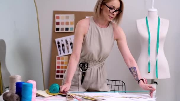 Švadlena s nůžkami na opasek drží zelenou nit v módním ateliéru návrhář s brýlemi vybírá šicí materiál pro makrame řemesla v dílně oděvy výroba - Záběry, video