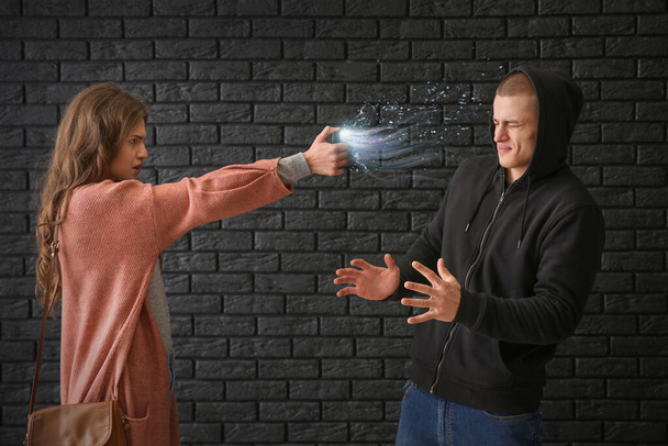 Woman with pepper spray defending herself against thief on dark background - Photo, Image