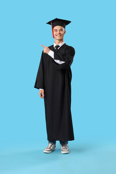 Male graduate student pointing at something on blue background - Fotoğraf, Görsel