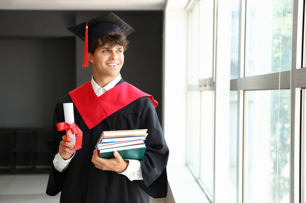 mężczyzna absolwent student z dyplomem i książki w pobliżu okna w pokoju - Zdjęcie, obraz