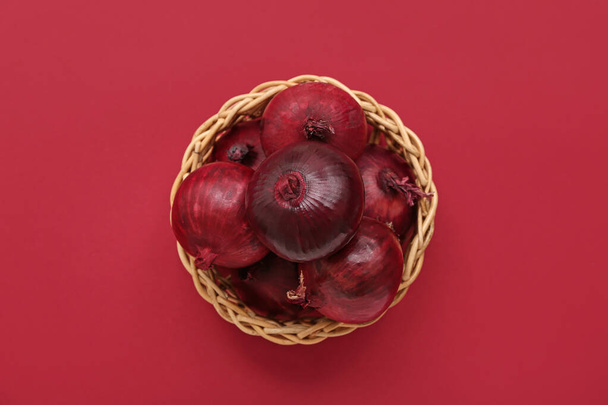 Cuenco de mimbre con cebollas rojas frescas sobre fondo de color - Foto, Imagen