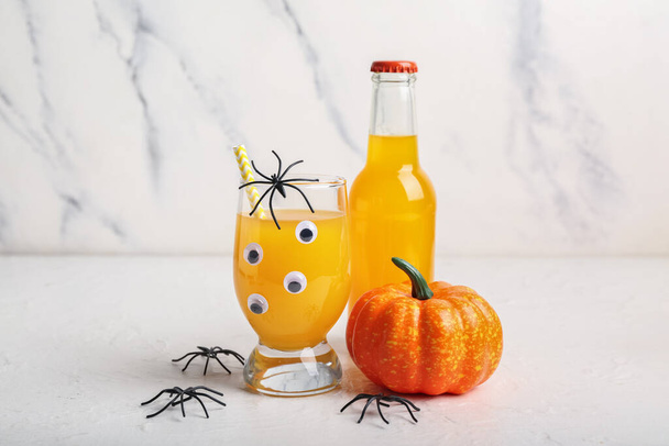 Glas en fles heerlijke oranje cocktail voor Halloween met spinnen op lichte achtergrond, close-up - Foto, afbeelding