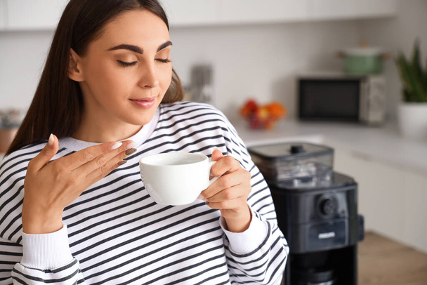 Молодая женщина с чашкой горячего кофе на кухне, крупным планом - Фото, изображение