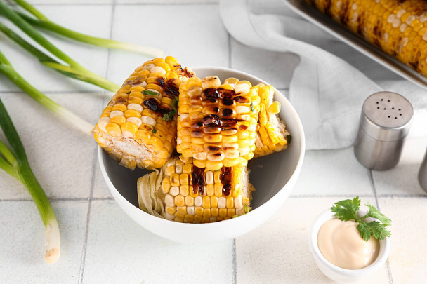 Bowl with tasty grilled corn cobs and green onion on white tile table - Photo, Image