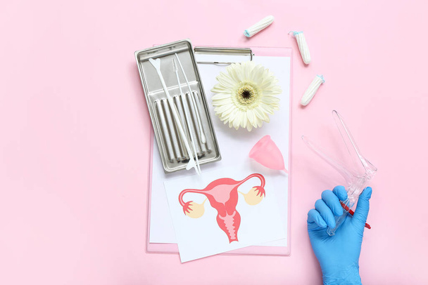 Main dans le gant médical, avec spéculum gynécologique, outils de test de frottis de pap, dessin de l'utérus féminin, coupe menstruelle et tampons sur fond rose - Photo, image