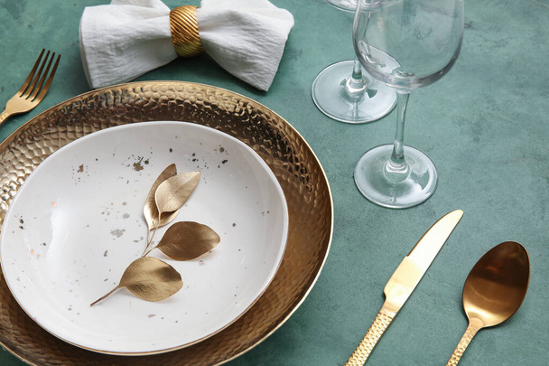 Elegáns asztaldíszítés arany levelekkel és evőeszközökkel a zöld asztalon - Fotó, kép