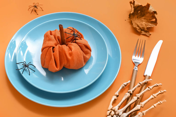 Festive table setting with Halloween pumpkin and skeleton hand on orange background - Photo, Image