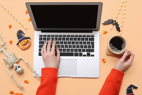 Mains féminines avec ordinateur portable, café et décorations d'Halloween sur fond beige - Photo, image