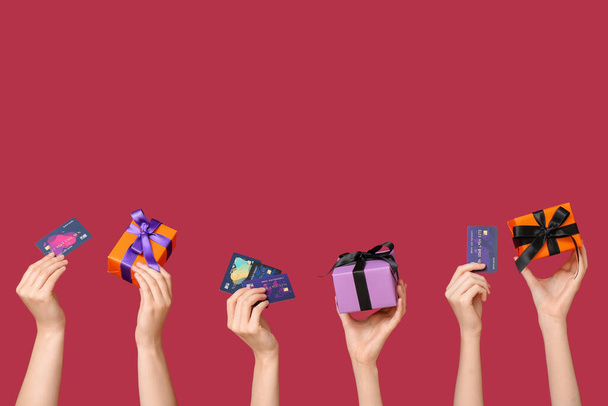 Mani femminili in possesso di regali di Halloween e carte di credito su sfondo rosso - Foto, immagini