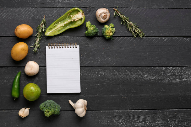Cuaderno en blanco con verduras frescas sobre mesa de madera negra - Foto, imagen