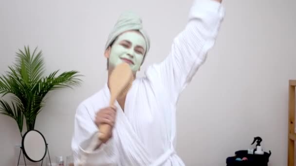 Bademantel-Karaoke: Eine fröhliche Dame, Tonmaske im Gesicht, singt in ein Haarbürstenmikrofon, tanzt zu Hause mit einem Handtuch auf dem Kopf und hat Spaß.  - Filmmaterial, Video