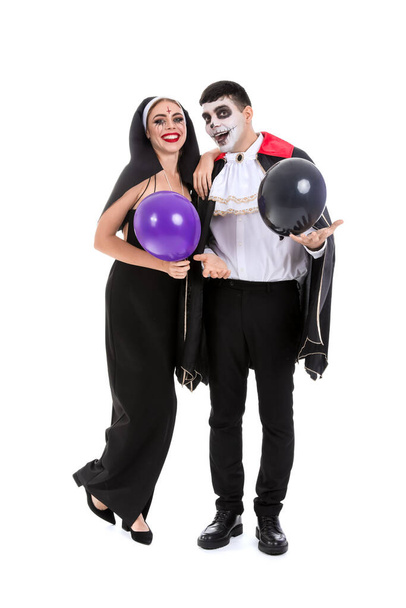 Junges Paar in Kostümen für Halloween-Party mit Luftballons auf weißem Hintergrund - Foto, Bild