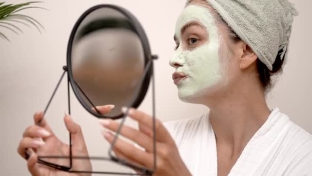 Clay Mask Delight: Sonriendo en su vestido, se entrega a un día de mimos, limpiando su piel facial con una máscara de arcilla verde casera, reflejos de espejo de alegría.  - Metraje, vídeo