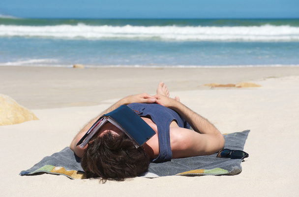 Мужчина спит на уединенном пляже с книжным покрывалом на лице
 - Фото, изображение