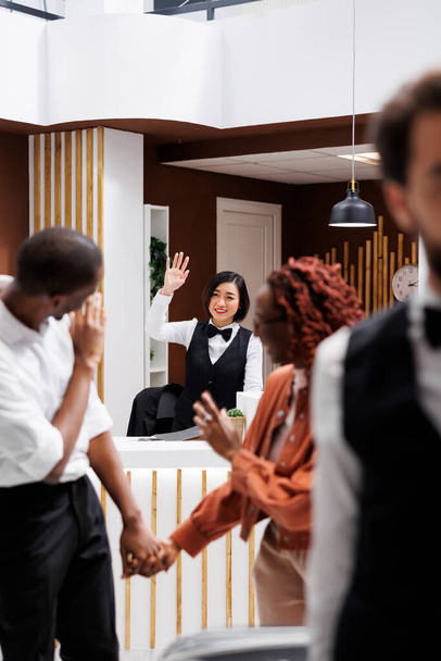 Ζευγάρι λέει αντίο σε υπάλληλο του ξενοδοχείου, front desk προσωπικό χαιρετά τους τουρίστες μετά την διαμονή τους στο σύγχρονο θέρετρο με υπηρεσίες πολυτελείας. Νέοι επισκέπτες check out από το δωμάτιο, υπηρεσία στέγασης. - Φωτογραφία, εικόνα