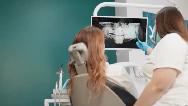 Nello studio dentistico, la paziente esamina immagini dettagliate della sua dentizione. Il dentista effettua un'analisi dettagliata e spiega la condizione dei denti sui raggi X e panorami della tomografia - Filmati, video