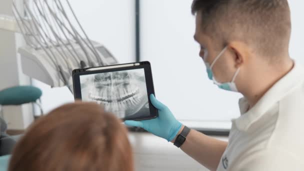 Le dentiste montre les résultats de la tomographie panoramique des dents des patients sur un comprimé. La patiente reçoit un examen, une consultation et un plan de traitement pour sa cavité buccale à l'aide d'une radiographie. Haut - Séquence, vidéo