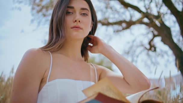 Barna modell olvasókönyv rét természet portré. Fiatal gyönyörű nő néz kamera megható haj búza mező piknik közelkép. Női hölgy pihen nyári táj essek új oldalak - Felvétel, videó