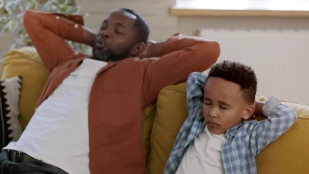 Szundikálás otthon. Pihent fekete férfi otthon meditál és megtanítja a kisfiát pihenni, ül a kanapén együtt csukott szemmel, nyomon követés lövés, lassított felvétel, szabad tér - Felvétel, videó