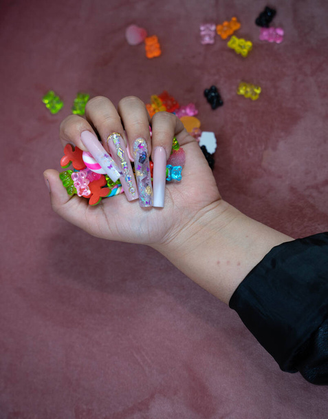 Mano de una mujer con uñas muy largas que aprieta con los dedos un montón de ositos de goma - Foto, imagen