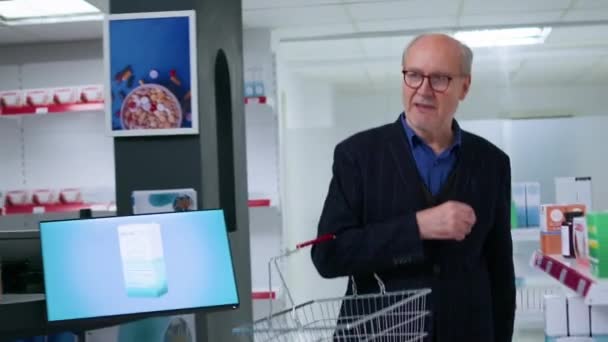 Kamerafahrt von älterem Mann mit Einkaufskorb, der Apotheke betritt, um Medikamente zur Herzinfarktprävention zu kaufen, und professionellen Apotheker um Hilfe bittet - Filmmaterial, Video