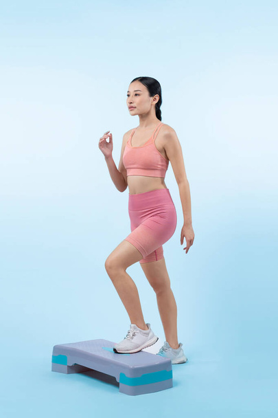 Vigorous energetic woman doing exercise at on studio short isolated background with cardio aerobic step workout. Young athletic asian woman dexterity and endurance training session concept. - Photo, Image