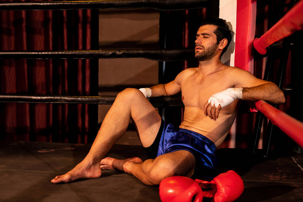 Tired and exhausted caucasian boxer removed his boxing glove and sitting, resting on the edge of the ring after intense training or fighting match. Impetus - Photo, Image
