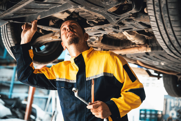 Araç tamircisi kaldırılmış aracın altından araba teftişi yapıyor. Üniformalı otomotiv teknisyeni araba akslarını ve şasi parçalarını dikkatle teşhis ediyor ve kontrol ediyor. Oxus. - Fotoğraf, Görsel