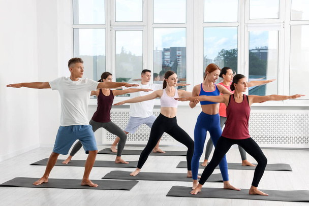 Yoga coach helpt vrouw tijdens groepsles binnen - Foto, afbeelding