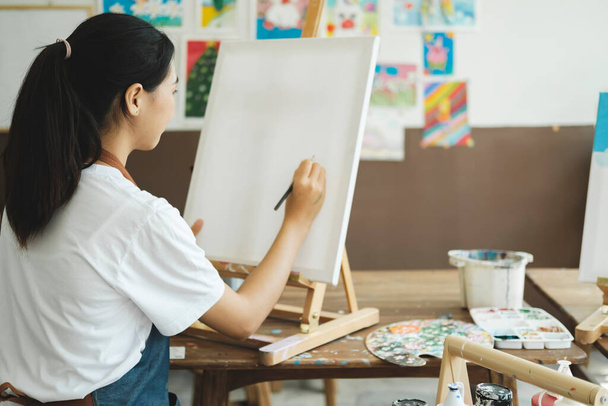 Die junge Künstlerin skizziert oder malt ihre Zeichnung in einer Atelierwerkstatt auf Leinwand. Ein Teenager-Mädchen, das Kunst und Zeichnung mag, nimmt sich Zeit, ihre Aquarelle mit großer Absicht auf Leinwand zu bringen - Foto, Bild