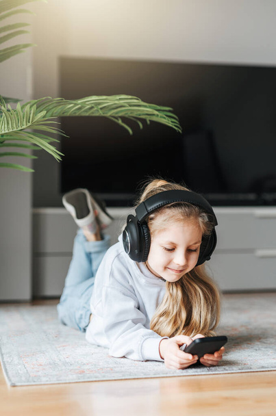Sorridente bambina ascoltando musica sdraiata sul pavimento
 - Foto, immagini