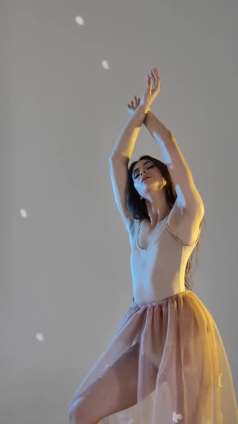 Genç bir kadın, dans eden bir balerin kız, yavaşça kollarını ve parmaklarını bir stüdyonun gri arka planında hareket ettiriyor, yavaş, orta boylu. Uzun saçlı, kahverengi saçlı kadın. Dikey video - Video, Çekim
