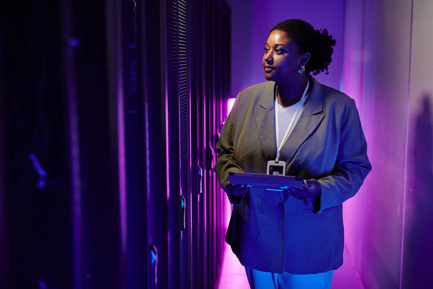 Portrait of female system administrator inspecting data network in server room lit by neon light, copy space - Photo, Image