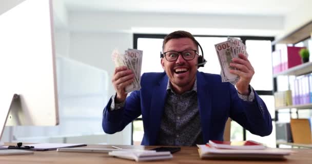 Sonriente operador de centro de llamadas rico sosteniendo y tirando pila de billetes de dólar. Ganancias remotas y llamadas a clientes - Imágenes, Vídeo