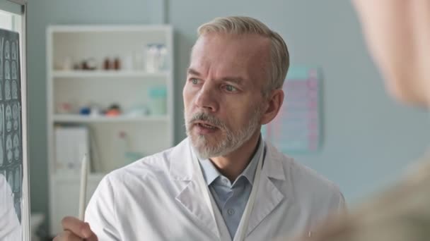 Egy középkorú férfi orvos válllövése felett, aki az MRI eredményeit tárgyalja a modern klinikán lévő beteggel. - Felvétel, videó