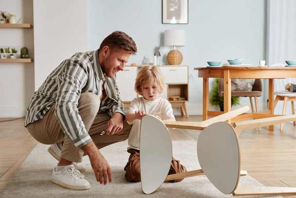 Full length portret van gelukkige vader en zoon monteren meubels samen in warm gezellig huis, kopieerruimte - Foto, afbeelding