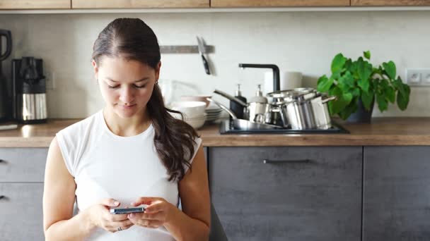 Nuori nainen istuu puhelimen kanssa keittiössä likaisten astioiden taustalla, hidastuminen, hidas elämä, viivyttely, konseptin lykkääminen. Laadukas 4k kuvamateriaalia - Materiaali, video