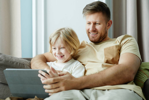 Ritratto di padre e figlio sorridente che guardano video online insieme e usano tablet mentre si rilassano sul divano a casa, copia lo spazio - Foto, immagini