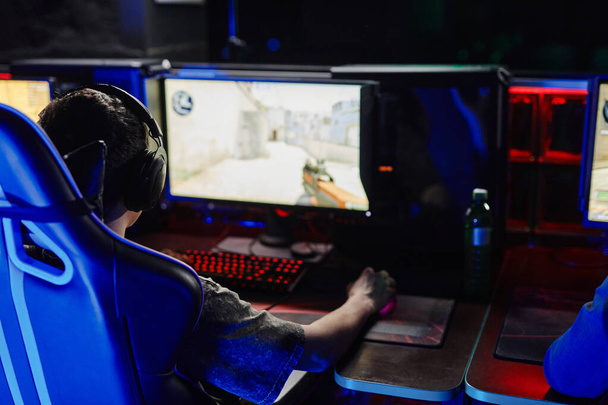 Zadní pohled na mladého muže hrát video hry střelec v tmě s kybernetickým týmem - Fotografie, Obrázek