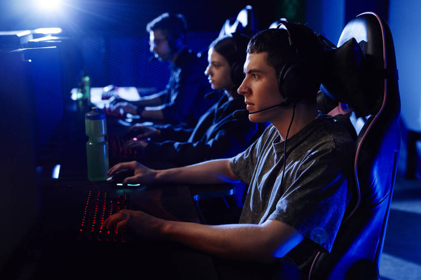 Seitenansicht Porträt von jungen Leuten, die im Cyber-Sportclub Videospiele hintereinander spielen, beleuchtet von Neonlichtern - Foto, Bild
