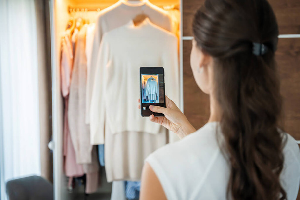 Mujer joven tomando fotos de ropa vieja no deseada para la venta en aplicación de teléfono inteligente. Foto de alta calidad - Foto, imagen