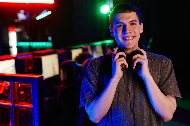 Obraz mladého muže v kybernetickém sportovním týmu, usmívající se na kameru vesele osvětlenou neonovým světlem, kopírovací prostor - Fotografie, Obrázek
