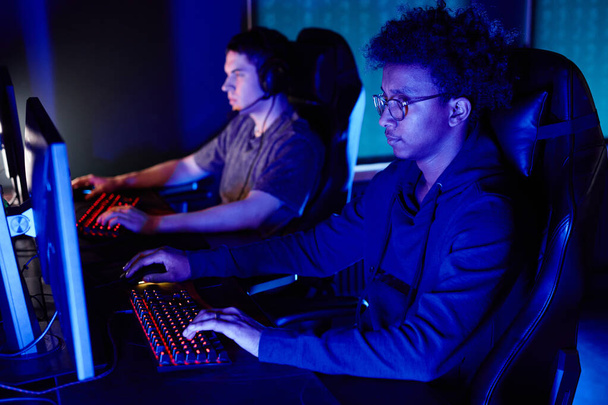 Mavi neon ışıklandırmalı siber spor kulübünde video oyunu oynayan siyahi bir adamın yan görünüm portresi - Fotoğraf, Görsel