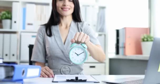 La empresaria seo o gerente está sosteniendo el despertador en el escritorio. Control del tiempo y gestión del tiempo - Imágenes, Vídeo
