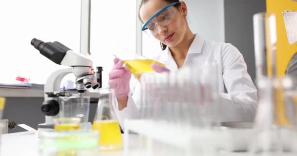 Chemist scientist looks at transparency of flask with yellow liquid or oil in chemical laboratory closeup. Research of oil products and fuels and lubricants - Footage, Video