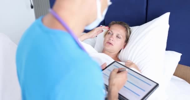 El médico toma notas en el comprimido del paciente y examina a la mujer paciente en la cama. Concepto de atención médica y seguro de salud - Metraje, vídeo